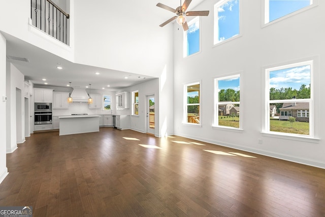 unfurnished living room featuring ceiling fan, dark hardwood / wood-style flooring, and a towering ceiling