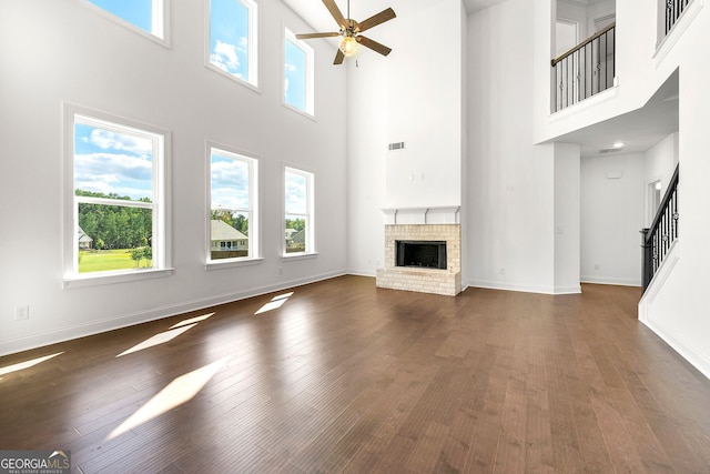 unfurnished living room with a high ceiling, a brick fireplace, ceiling fan, and dark wood-type flooring