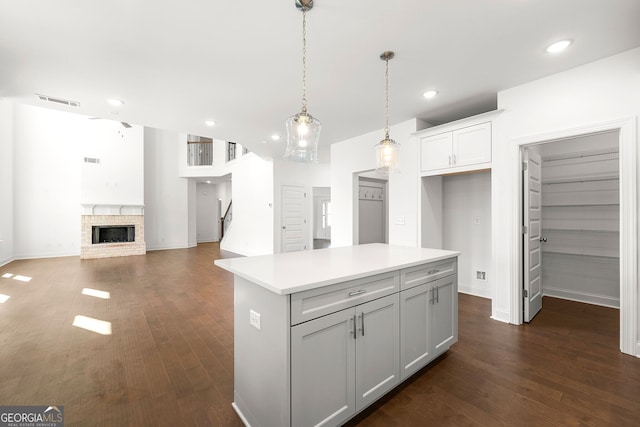 kitchen with gray cabinetry, a center island, hanging light fixtures, a brick fireplace, and dark hardwood / wood-style flooring