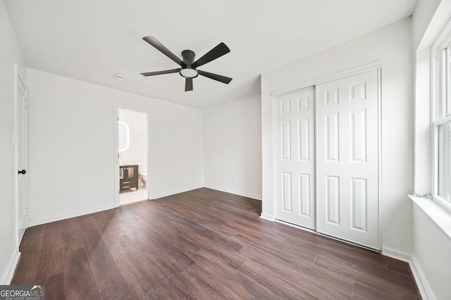 unfurnished bedroom with ensuite bathroom, ceiling fan, dark hardwood / wood-style floors, multiple windows, and a closet