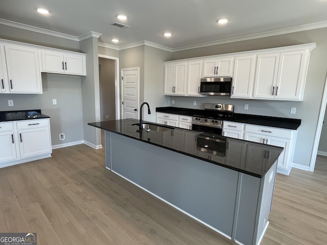 kitchen featuring dark countertops, appliances with stainless steel finishes, white cabinets, a kitchen island with sink, and a sink