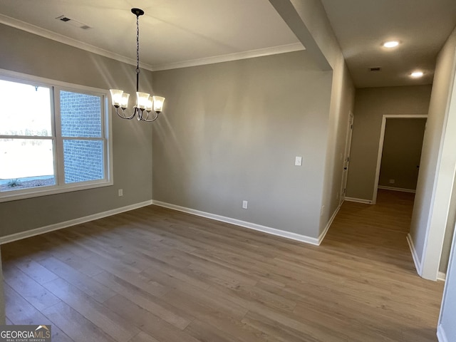 empty room with a notable chandelier, visible vents, ornamental molding, wood finished floors, and baseboards