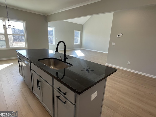 kitchen featuring decorative light fixtures, open floor plan, a kitchen island with sink, a sink, and dark stone counters