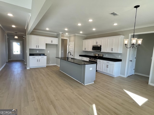 kitchen with stainless steel appliances, dark countertops, a kitchen island with sink, white cabinets, and a sink