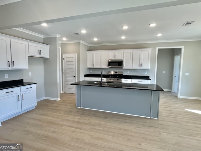 kitchen featuring a kitchen island with sink, appliances with stainless steel finishes, dark countertops, and white cabinetry