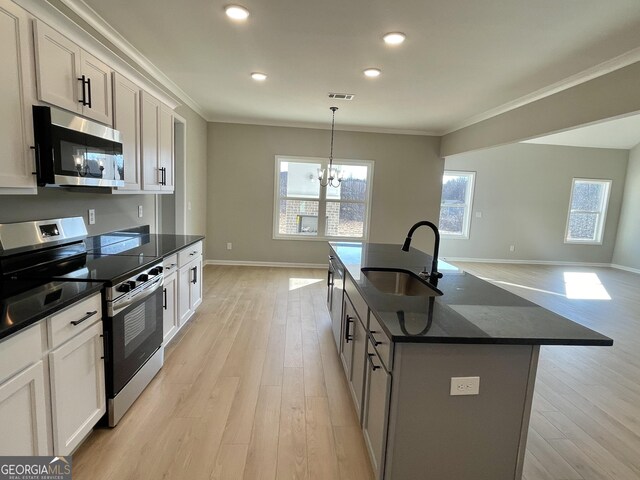 kitchen featuring decorative light fixtures, stainless steel appliances, visible vents, a sink, and an island with sink