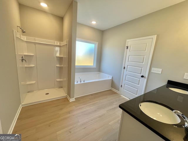 bathroom with double vanity, a stall shower, wood finished floors, a sink, and a bath