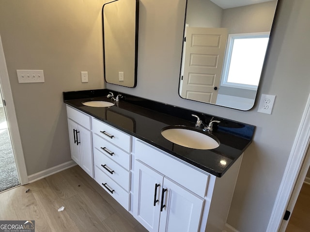 full bathroom featuring wood finished floors, a sink, baseboards, and double vanity