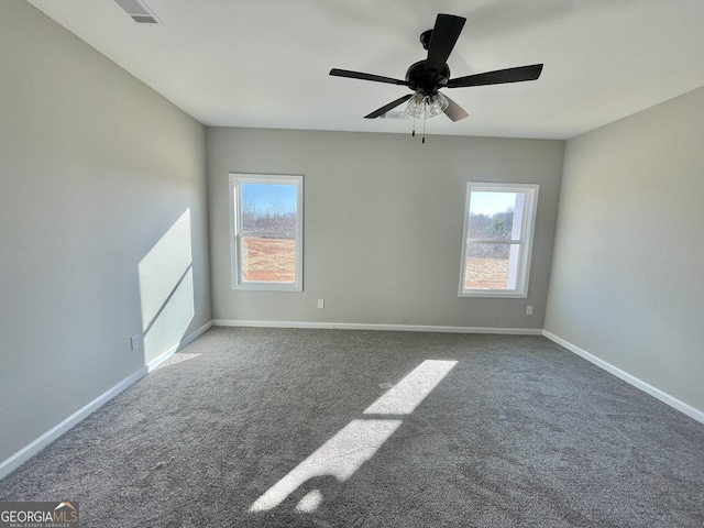 empty room with a healthy amount of sunlight, dark carpet, visible vents, and baseboards