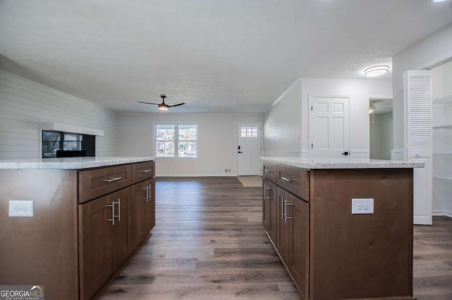 kitchen with ceiling fan, a kitchen island, dark wood-type flooring, and light stone counters