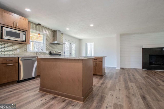 kitchen featuring appliances with stainless steel finishes, wall chimney exhaust hood, decorative light fixtures, hardwood / wood-style flooring, and a center island