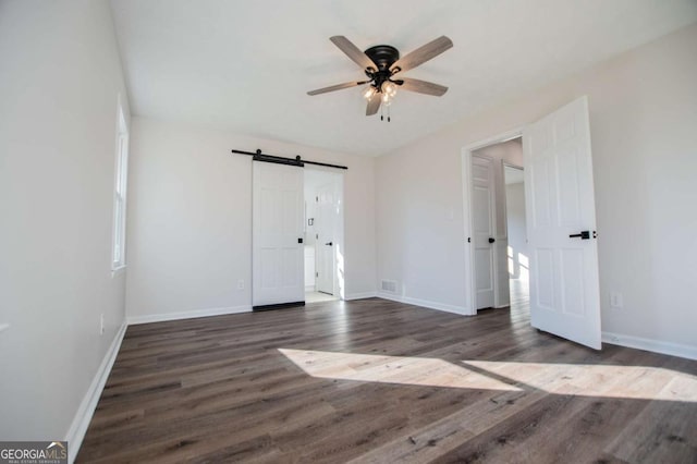 unfurnished bedroom featuring a barn door, ceiling fan, and dark hardwood / wood-style floors