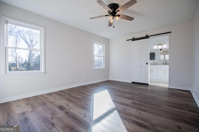 spare room with dark hardwood / wood-style floors, a barn door, plenty of natural light, and ceiling fan