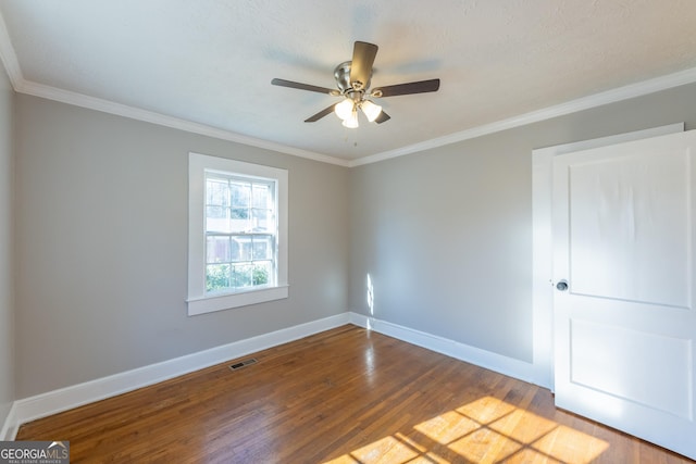 spare room with baseboards, crown molding, visible vents, and wood finished floors