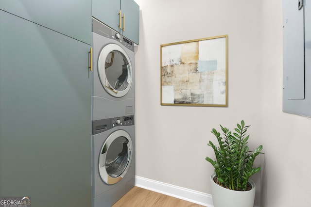 clothes washing area with cabinets, electric panel, light hardwood / wood-style flooring, and stacked washer and clothes dryer