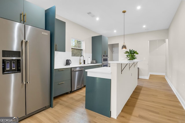 kitchen featuring light wood-type flooring, backsplash, stainless steel appliances, decorative light fixtures, and a kitchen island