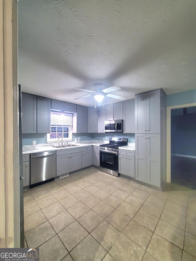 kitchen featuring stainless steel appliances, light countertops, gray cabinetry, a sink, and ceiling fan