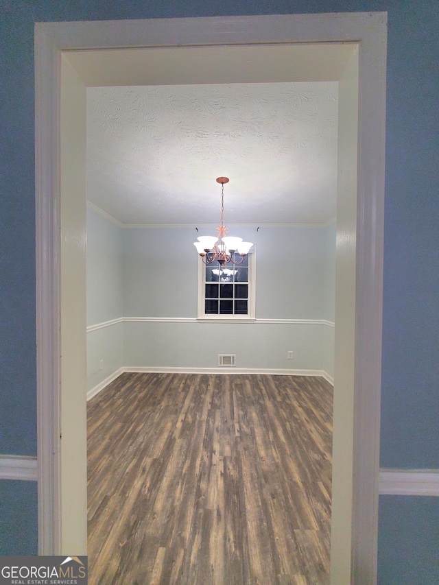 empty room with ornamental molding, an inviting chandelier, and dark wood-type flooring