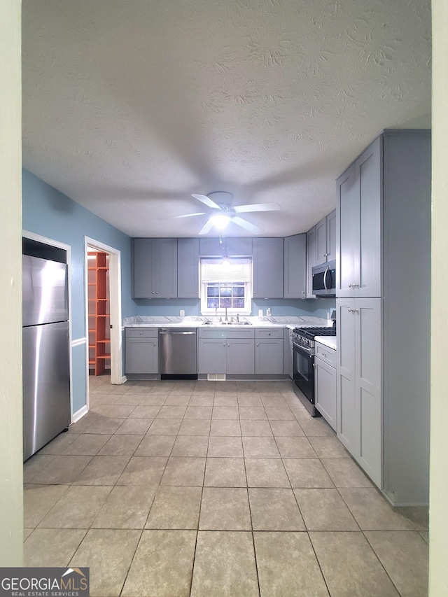 kitchen with gray cabinetry, ceiling fan, sink, light tile patterned floors, and appliances with stainless steel finishes