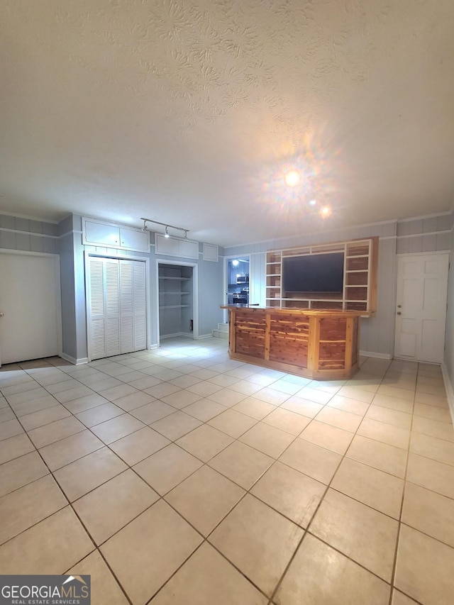 unfurnished living room featuring light tile patterned floors, built in shelves, a textured ceiling, and rail lighting