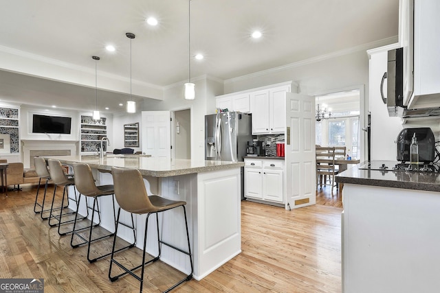 kitchen with white cabinets, stainless steel fridge, an island with sink, black cooktop, and decorative light fixtures