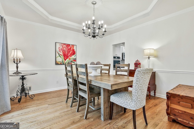 dining area with a tray ceiling, light hardwood / wood-style flooring, a chandelier, and ornamental molding