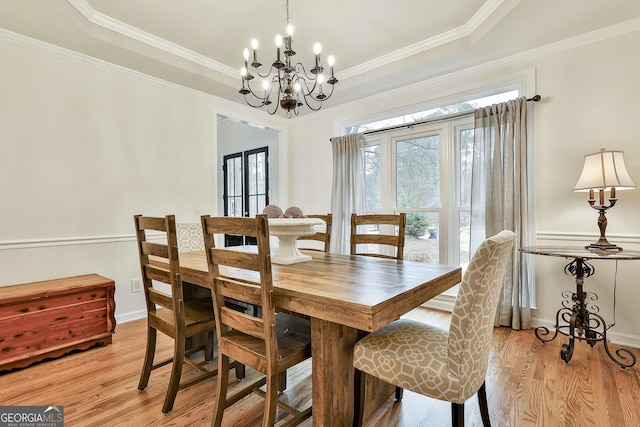 dining space with crown molding, light hardwood / wood-style flooring, a tray ceiling, and a chandelier