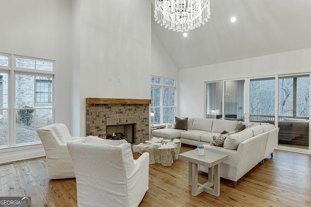 living room featuring a high ceiling, a brick fireplace, a chandelier, and light hardwood / wood-style floors