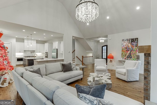 living room with hardwood / wood-style flooring, sink, a notable chandelier, and high vaulted ceiling