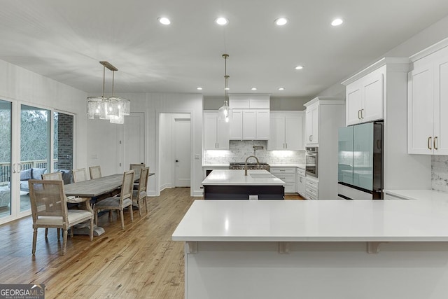 kitchen featuring white cabinetry, hanging light fixtures, fridge, stainless steel oven, and a center island with sink