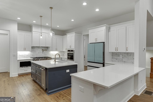 kitchen with pendant lighting, sink, stainless steel appliances, white cabinets, and a center island with sink