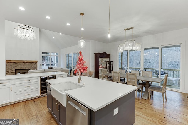 kitchen with sink, white cabinetry, decorative light fixtures, stainless steel dishwasher, and a kitchen island with sink