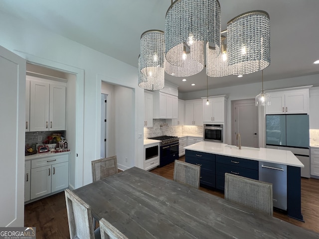 kitchen with dark wood-type flooring, hanging light fixtures, an island with sink, stainless steel appliances, and white cabinets