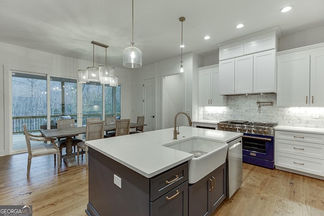 kitchen featuring appliances with stainless steel finishes, an island with sink, sink, white cabinets, and hanging light fixtures