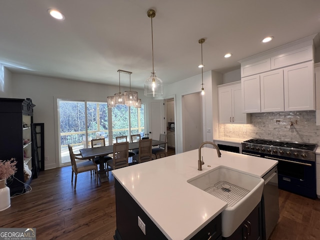 kitchen with pendant lighting, sink, a kitchen island with sink, white cabinets, and range with two ovens