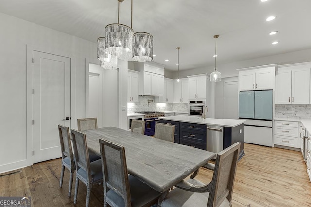 kitchen with a kitchen island with sink, decorative light fixtures, white cabinets, and appliances with stainless steel finishes