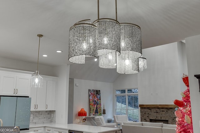 room details with stainless steel fridge, hanging light fixtures, white cabinets, a brick fireplace, and decorative backsplash