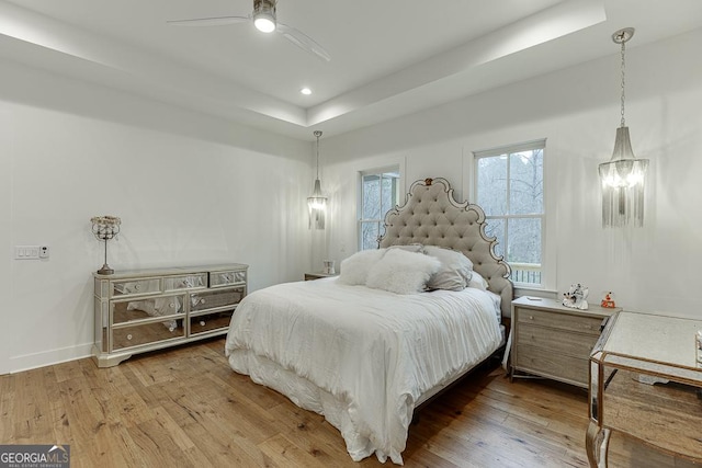 bedroom with hardwood / wood-style flooring, ceiling fan, and a raised ceiling