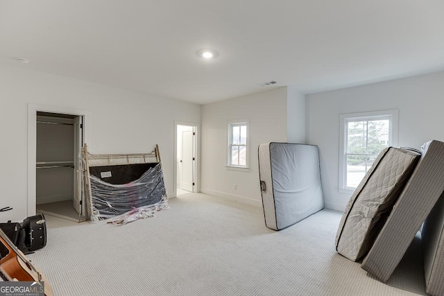 carpeted bedroom featuring a walk in closet and multiple windows