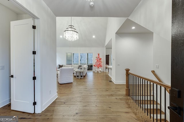 corridor featuring an inviting chandelier, vaulted ceiling, and light wood-type flooring