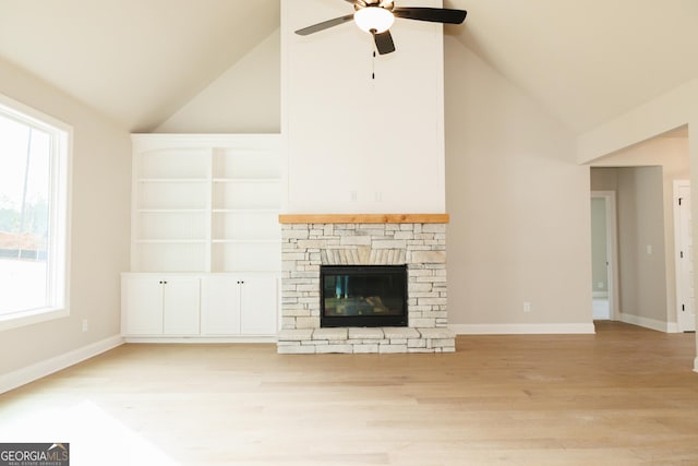 unfurnished living room with ceiling fan, a stone fireplace, high vaulted ceiling, and light hardwood / wood-style flooring