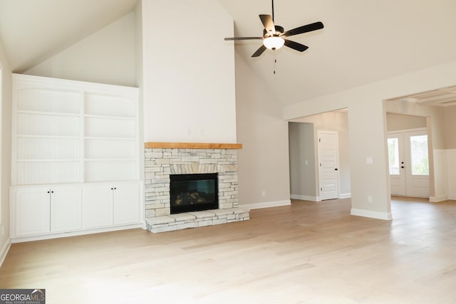 unfurnished living room with french doors, a stone fireplace, high vaulted ceiling, light hardwood / wood-style flooring, and ceiling fan