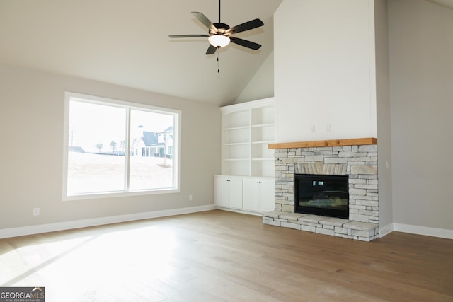 unfurnished living room featuring built in shelves, a stone fireplace, high vaulted ceiling, hardwood / wood-style flooring, and ceiling fan