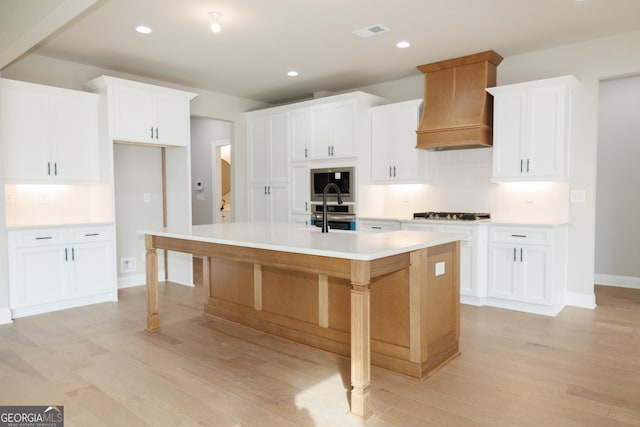 kitchen featuring white cabinets, custom exhaust hood, and a center island with sink