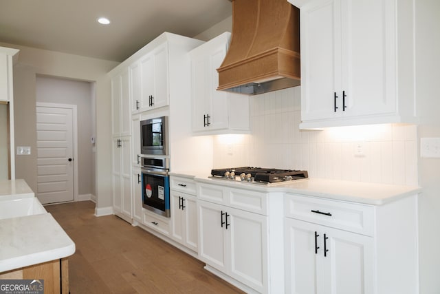 kitchen with stainless steel appliances, premium range hood, white cabinets, and backsplash