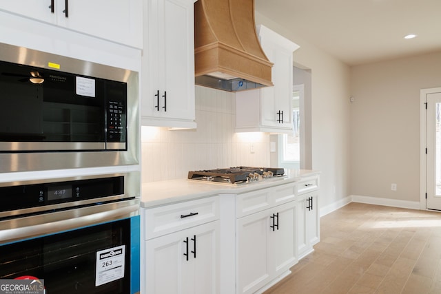 kitchen featuring premium range hood, appliances with stainless steel finishes, decorative backsplash, and white cabinets