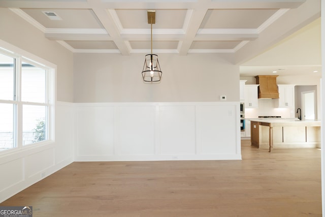 unfurnished dining area featuring beam ceiling, ornamental molding, coffered ceiling, and light hardwood / wood-style floors