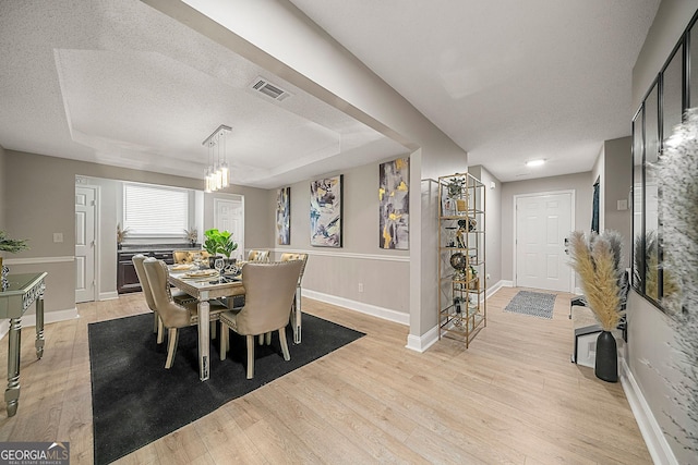 dining space with a tray ceiling, light hardwood / wood-style flooring, and a textured ceiling