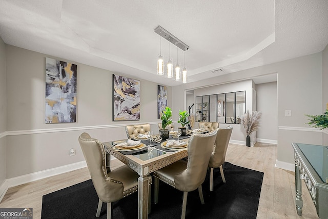 dining room with a raised ceiling, light wood-type flooring, a textured ceiling, and an inviting chandelier