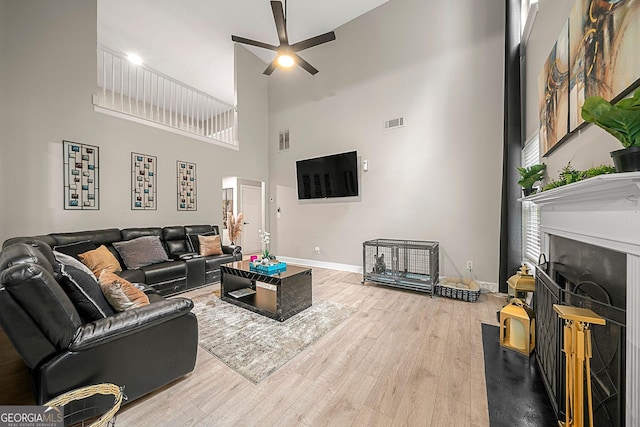 living room featuring ceiling fan, a towering ceiling, and wood-type flooring